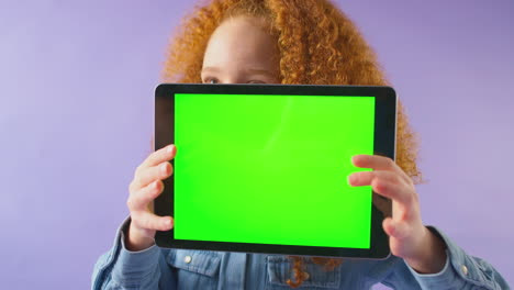 studio portrait of girl using digital tablet with green screen against purple background