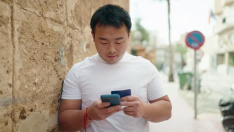 young chinese man using smartphone and credit card at street