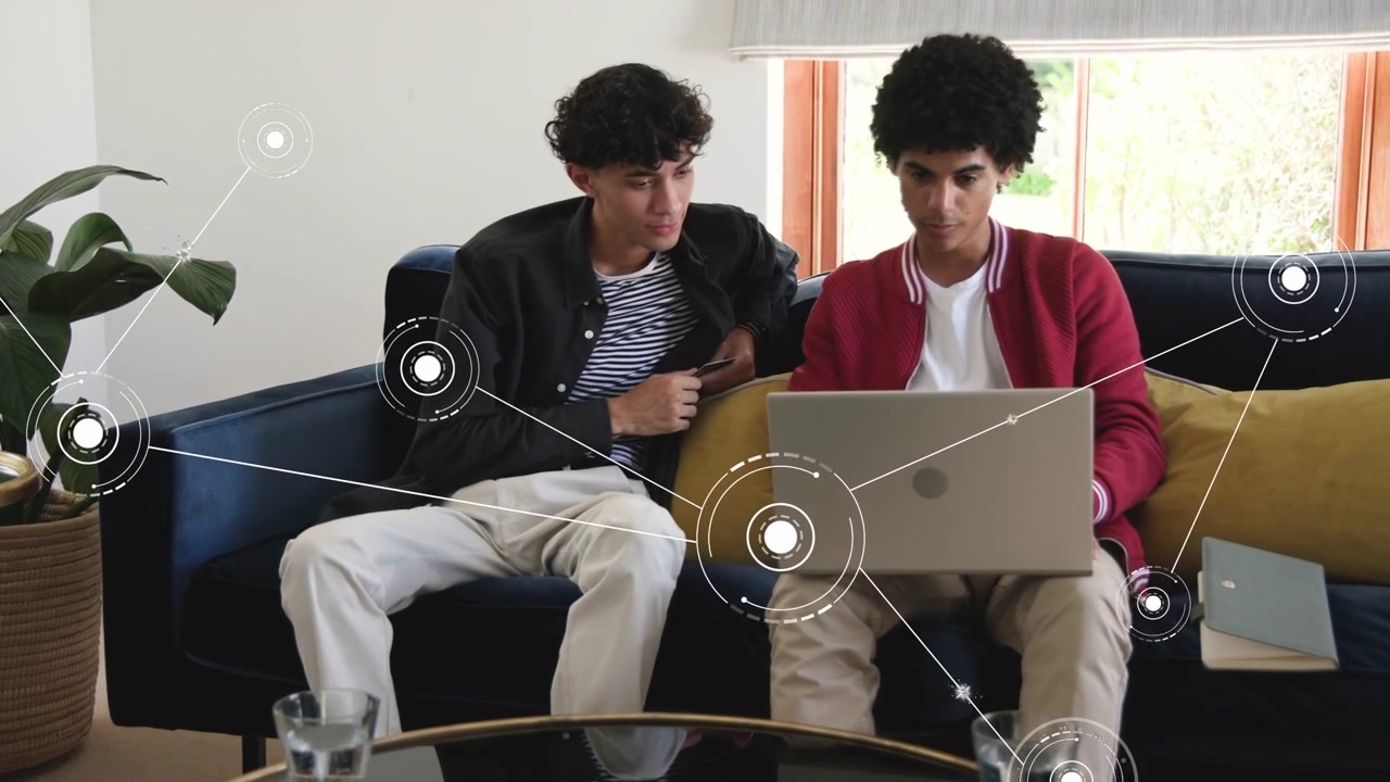 Red-jacket man lifting laptop, peer leaning in, HUD linking data to laptop, collaborating on tech