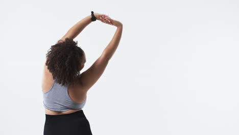 Biracial beautiful plus size woman stretching in grey sports bra and black leggings