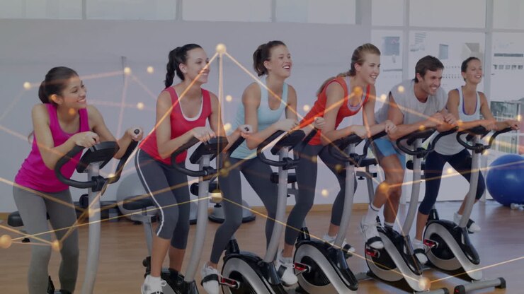 Six adults pedaling stationary bikes in fitness studio, glowing network lines showing health data