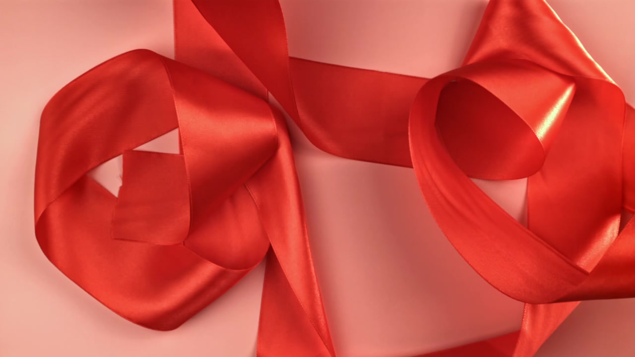 Elegantes rotes Satinband, dekorativ auf rosa Hintergrund arrangiert.
