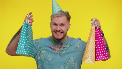 hombre con un sombrero de fiesta y cargando bolsas de regalos sonriendo felizmente