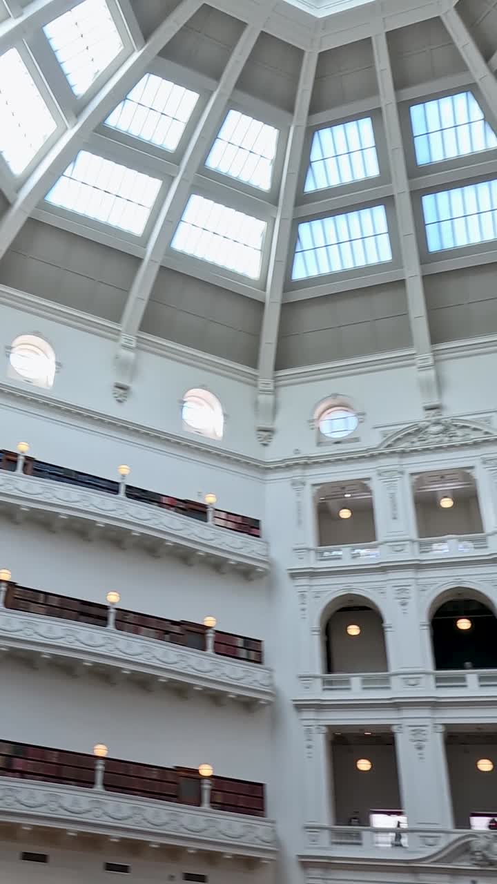 Un'inquadratura verticale dal basso che mostra l'architettura bianca e ornata e il lucernario di una biblioteca storica.