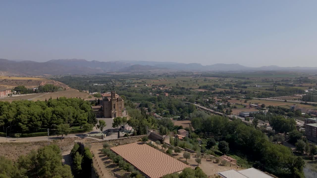A captivating far-distance drone circular shot captures the beauty of the Catholic Church Santa Maria de Balaguer in Lleida, Spain, as it gleams in the warm afternoon sun