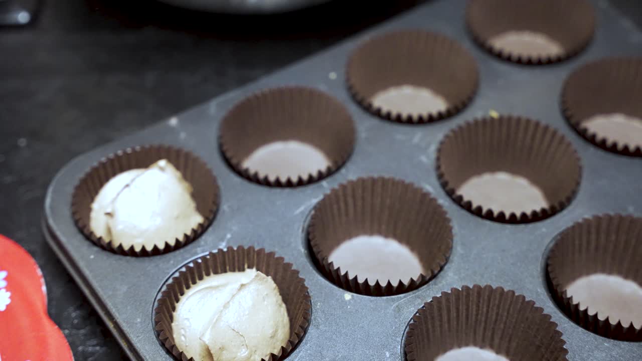 Preparation of cupcake batter using a scoop to fill the lined baking tray.