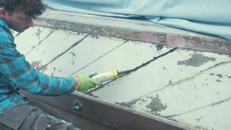 a young man sealing hull planks of a boat with sealant