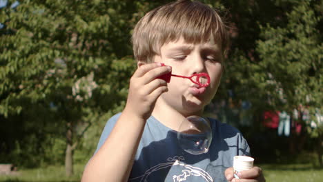 Little-boy-blows-bubbles-in-slow-motion-on-summer-day,-close-up