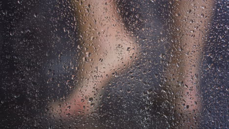 Woman-feet-behind-shower-cabin-misted-glass-with-water-drops