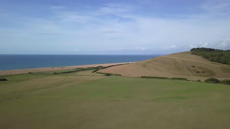 low forward tracking aerial moving upwards over a field revealing the vast expans of the dorset coastline at the west end of chesil beach