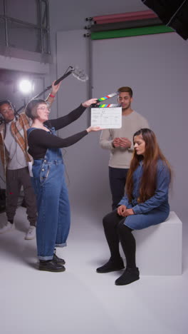 video vertical de asistente de producción femenina usando clapperboard mientras los actores filman una película o video en el estudio con el equipo de filmación filmado en tiempo real