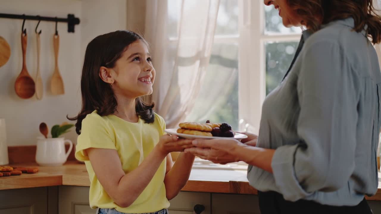 Madre in maglietta blu che porge pancake con frutti di bosco in cucina mentre il bambino allunga la mano per prendere il cibo