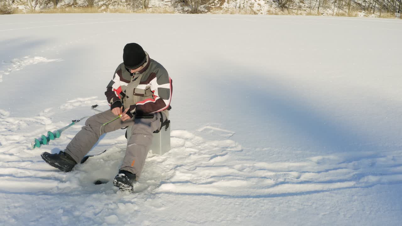 el hombre que sostiene la caña está pescando en un agujero de hielo en el lago congelado durante el invierno soleado