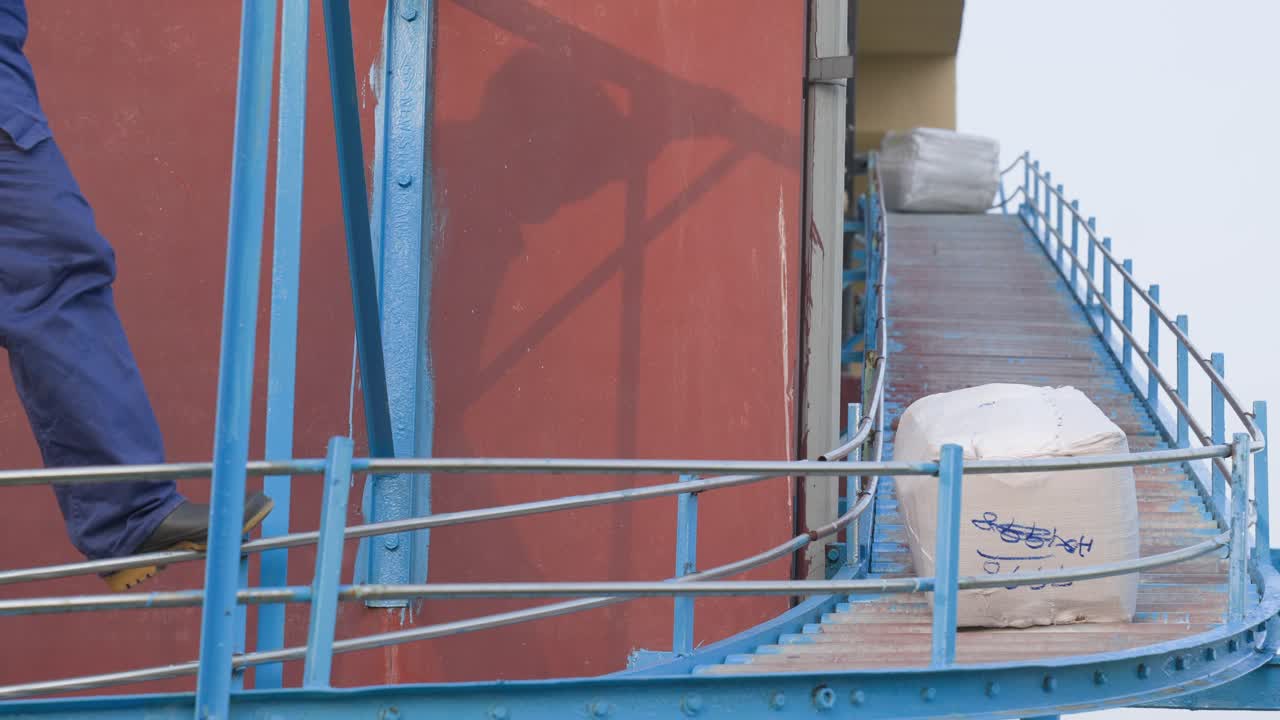 Leather Factory Worker Collecting Packages Of Products From A Outdoor Industrial Conveyor Belt.