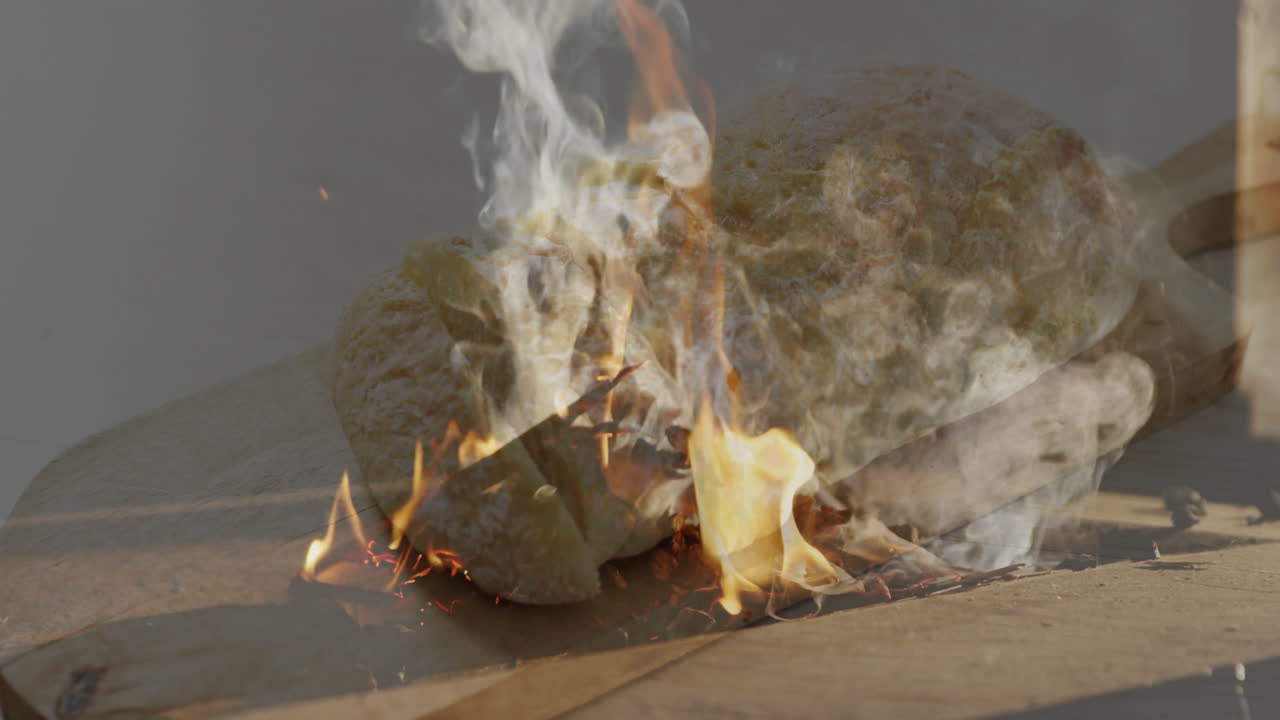 Baking bread over open flames, smoke rising in rustic outdoor setting