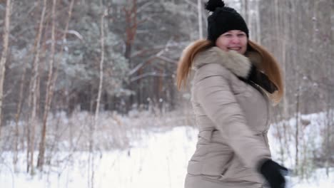 red-haired girl throws snow to the top, smiling, and dancing in winter forest in warm clothes: black hat and light jacket, 4k. blurred forest background