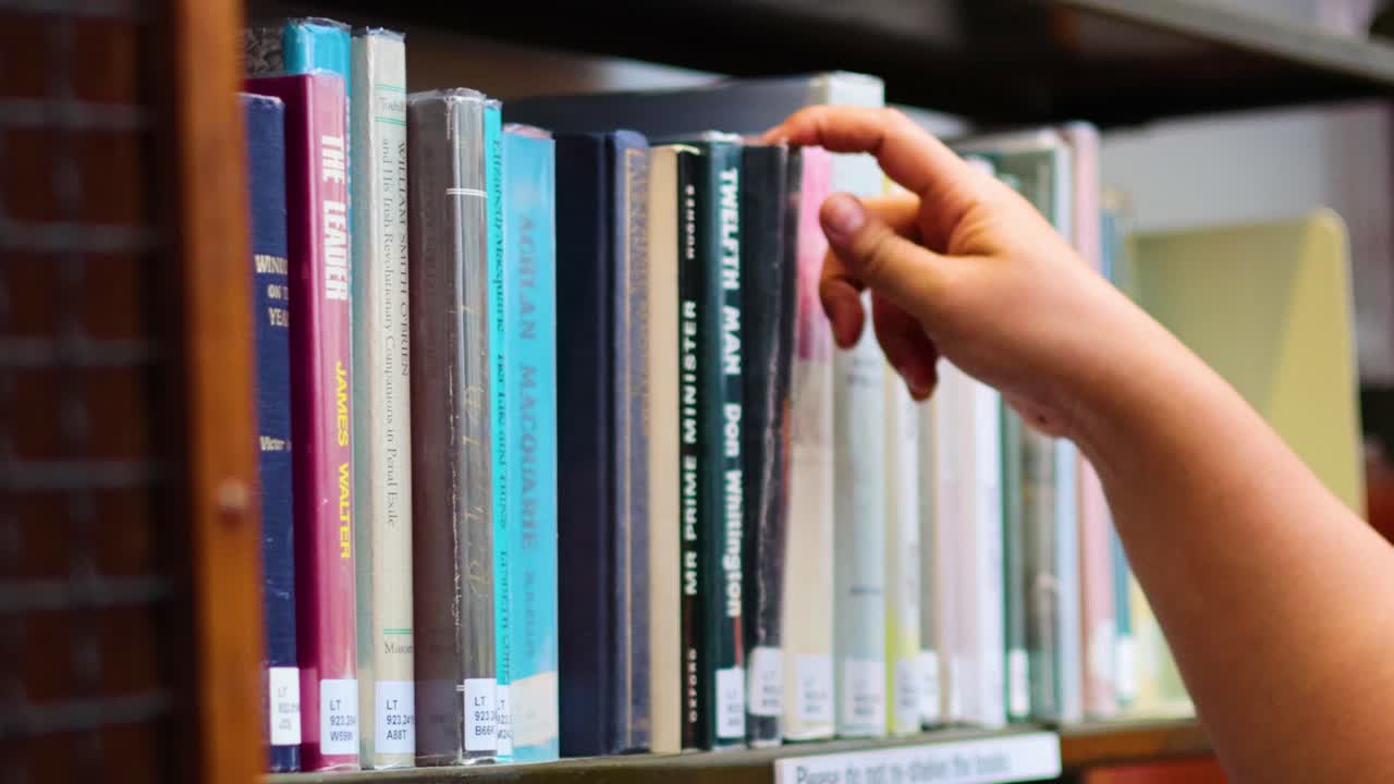 eligiendo a mano un libro de la estantería de la biblioteca