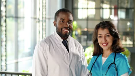 portrait of mixed-race male and female doctors in uniforms smiling joyfully at camera in a clinic