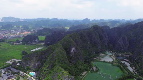 drone pan right across tall jagged limestone ridge surrounded by lush greenery and small ponds in ninh binh