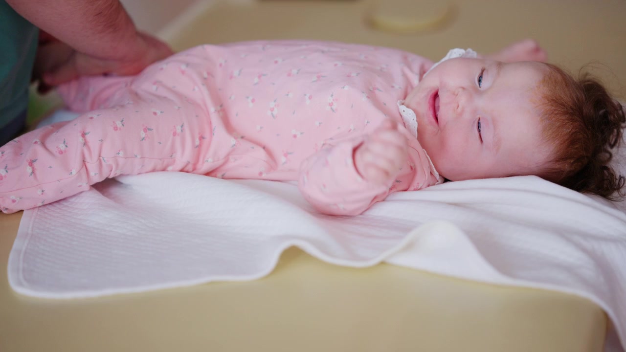 Primo piano di un neonato sdraiato su un lettino da trattamento mentre un adulto sostiene delicatamente il bambino.