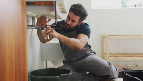 fontanero trabajando para arreglar el fregadero con fugas en el baño de la casa