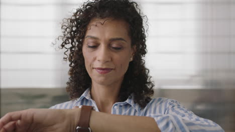 portrait of mature hispanic business woman checking messages online using smart watch mobile technology in office background