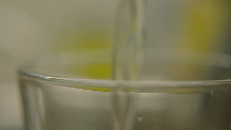agua que fluye en un vidrio transparente, capturado en detalle con un fondo borroso y de tonos suaves.