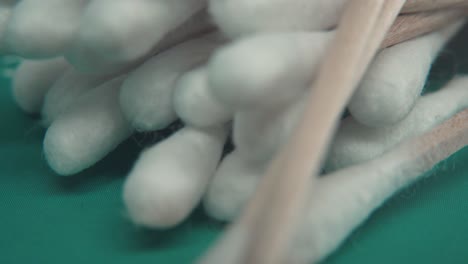 A-slow-smooth-detailed-macro-tilt-up-shot-of-a-pile-of-Q-tips,-white-soft-cotton-tips,-brown-wooden-sticks,-professional-studio-lighting,-green-background,-4k-video