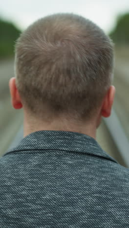 una vista de cabeza de un hombre anciano caminando solo por una vía ferroviaria, mirando a su alrededor con vista de bokeh de árboles y postes eléctricos