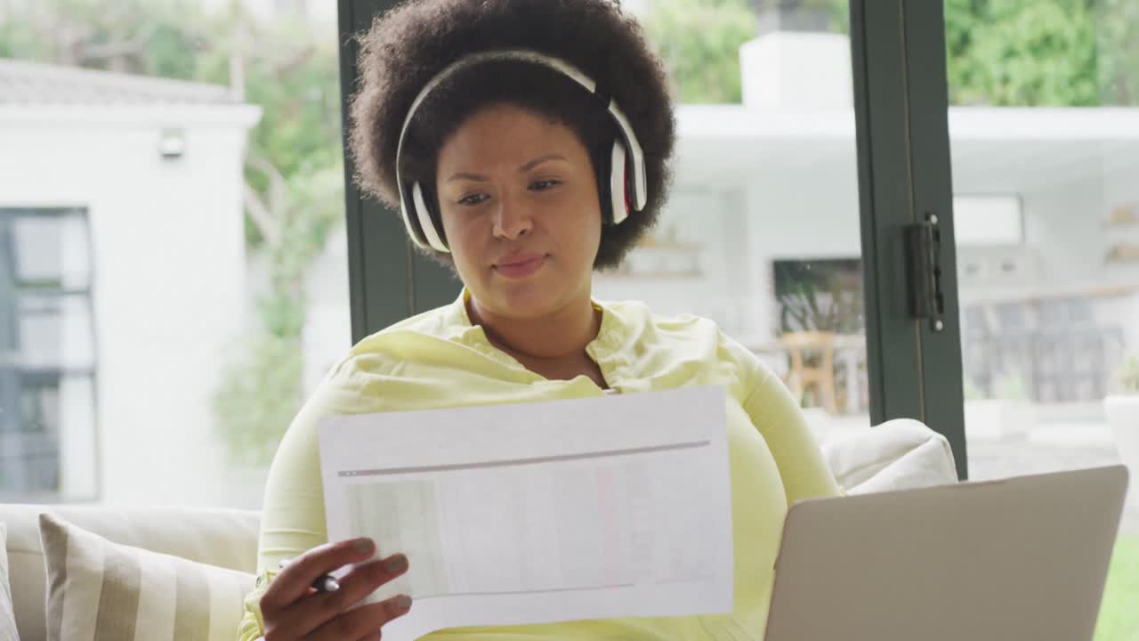 Video di una donna afroamericana taglia forte e felice con le cuffie seduta sul divano con il laptop.