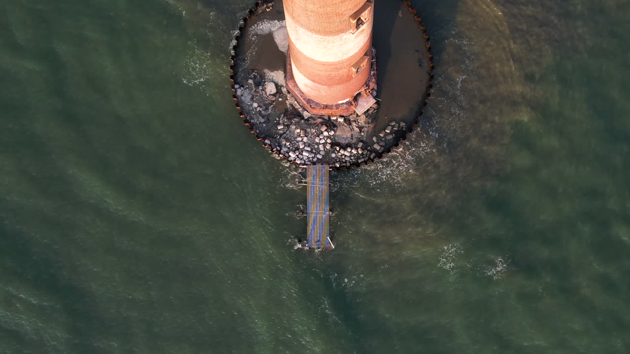 A drone shot panning out to a lighthouse that is surrounded by the ocean.