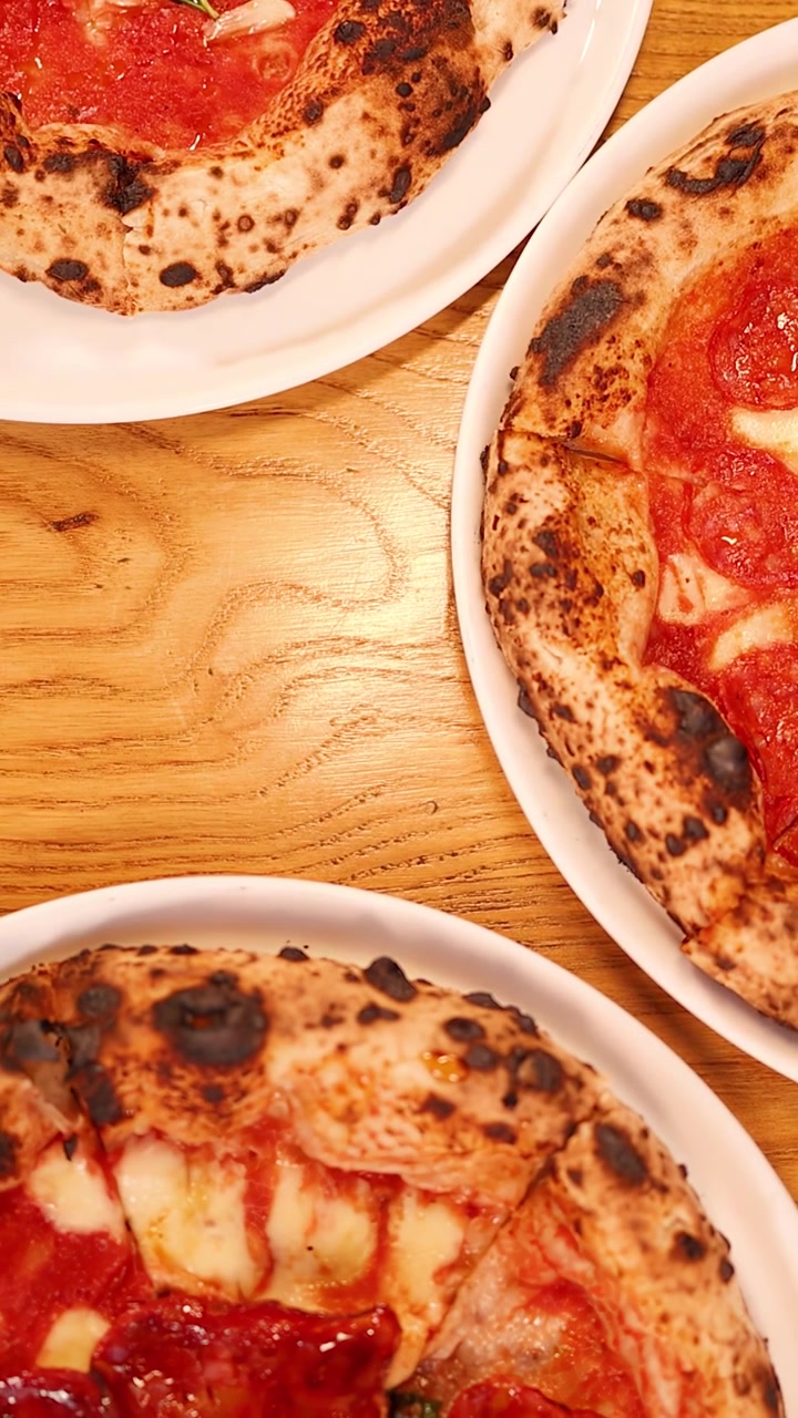 Kamera panorerer ovenfra over pepperoni-pizzaer, ristet brød og ost på et træbord