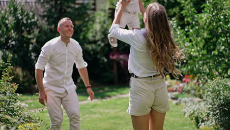smiling loving dad walks behind his son learning to walk in the garden. mother stretches her arms to her beloved baby. woman picks up a kid and tosses him up.