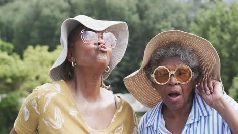 retrato de felices amigas afroamericanas mayores haciendo caras divertidas en el jardín, en cámara lenta