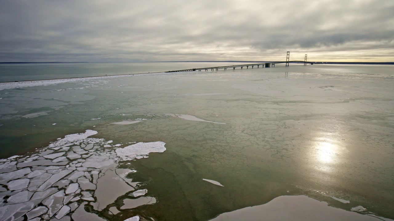 Dronebilde av Mackinac Bridge om vinteren med snødekte isklumper i forgrunnen