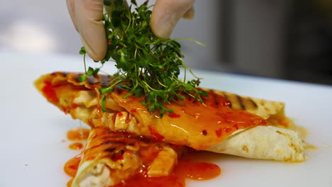 Delicious pita poured with sauce. Cook decorates a dish with green sprouts. Before serving a meal, the chef of the restaurant completes the decoration.Close-up.