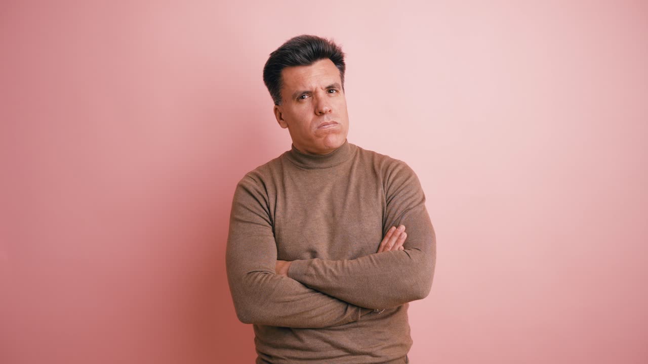 Serious Man with Arms Crossed Looking at Camera on Pink Background