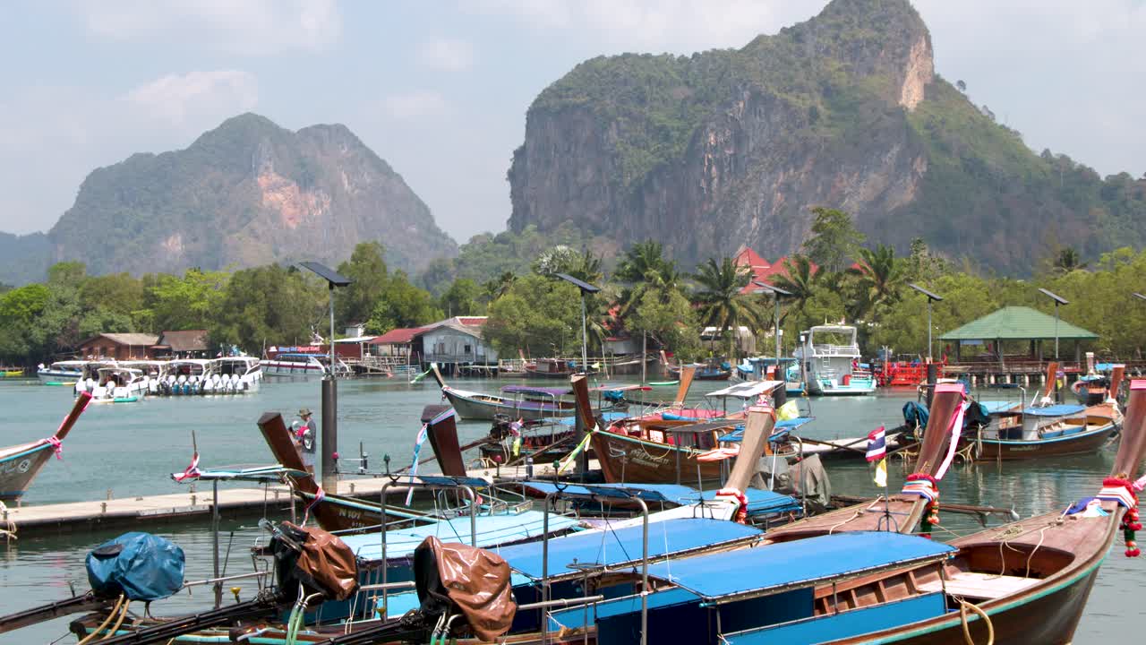 Cảnh quay tĩnh góc rộng những chiếc thuyền đuôi dài bằng gỗ đang neo đậu trong làn nước màu ngọc lam dưới ánh nắng nhiệt đới rực rỡ.