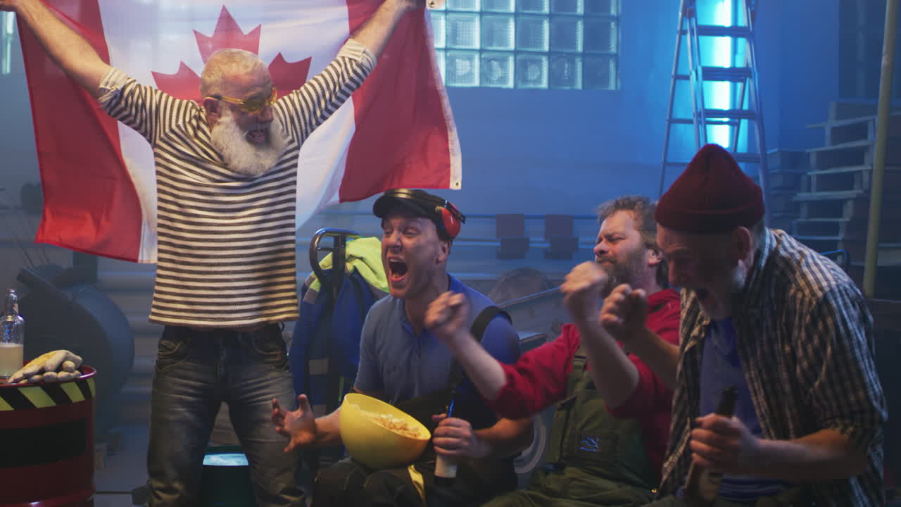 Excited men celebrating a game with a Canadian flag in an industrial setting
