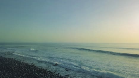 Shot-overlooking-breaking-waves-on-black-volcanic-pebble-rocks-at-sunset-on-Madeira-island-coastline