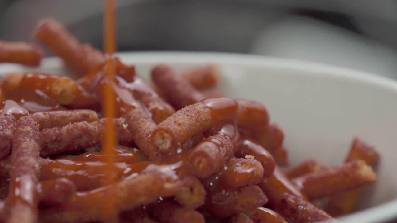 Adding red sauce to spicy chips while the plate rotates. Close-up