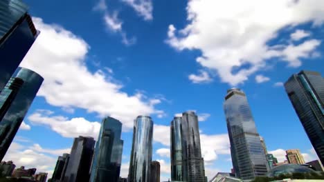 tall glass skyscrapers dominate the urban skyline, reaching toward a bright blue sky filled with fluffy clouds. the scene captures the modern architecture and vibrant atmosphere of the city.