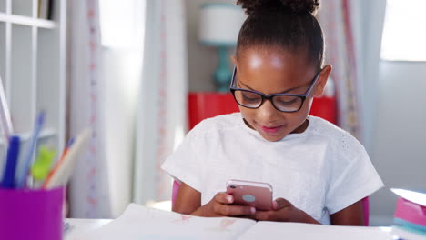 Una-Joven-Con-Gafas-Sentada-En-Un-Escritorio-En-El-Dormitorio-Jugando-En-El-Teléfono-Móvil