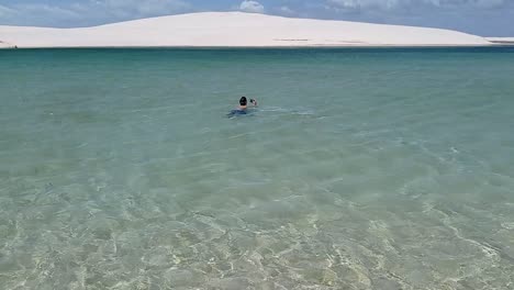 boy swimming on clear blue lagoon in lencois maranhenses national park, brazil