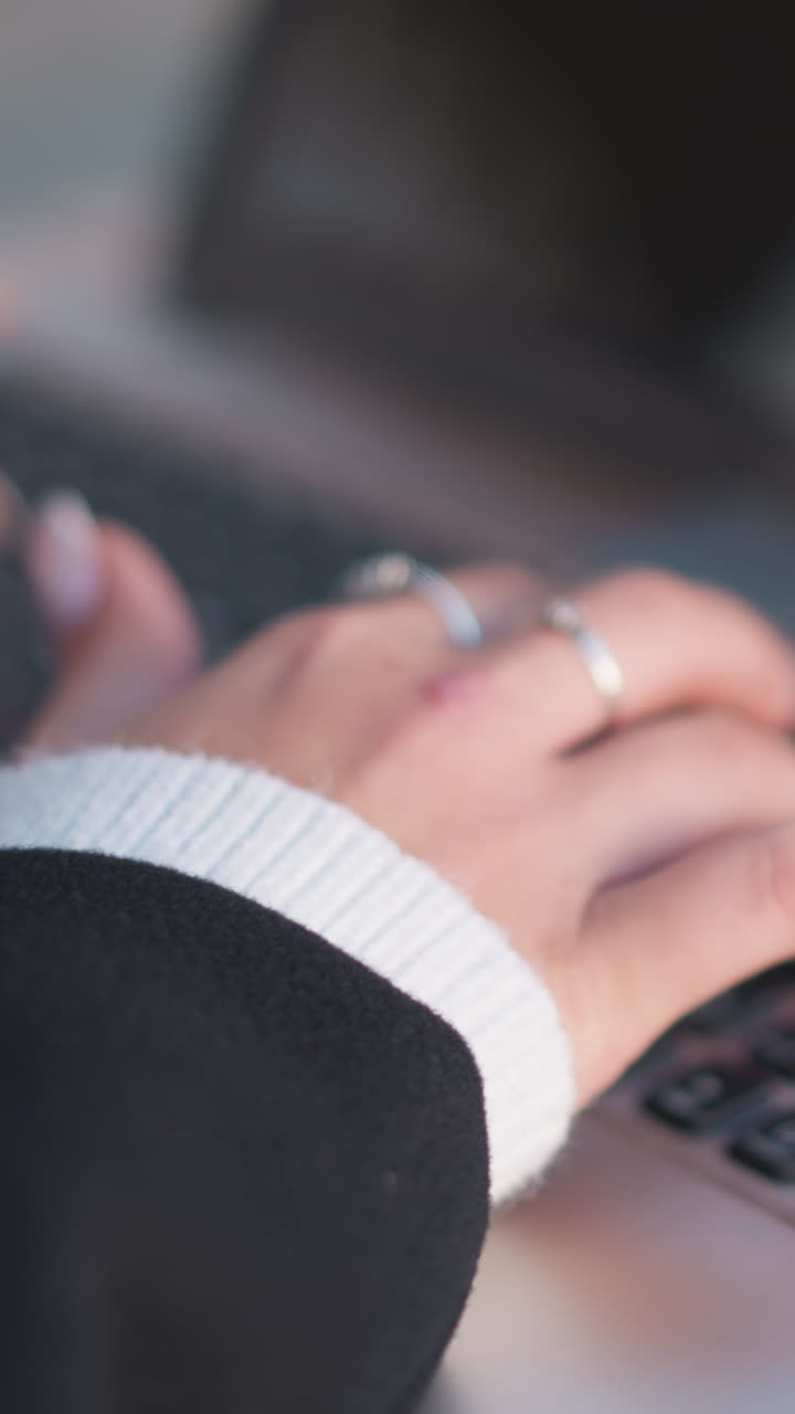 primer plano de manos adornadas con uñas pulidas y anillos delicados escribiendo en el teclado de la computadora portátil con un ligero borrón y reflejo de luz suave en la pantalla