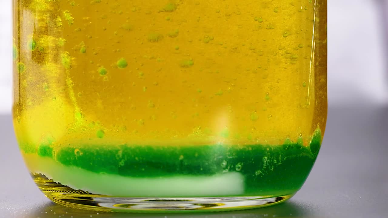 A close-up view of yellow and green liquids interacting at the bottom of a glass container.