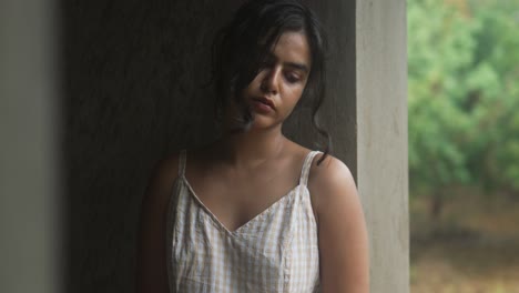 Young-woman-standing-by-a-window-with-soft-natural-light,-looking-thoughtfully-off-camera