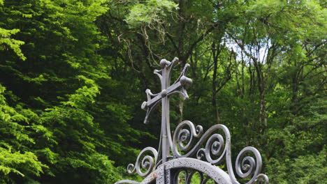 zoom in on a somber catholic cross on a ornamental fence, hidden in wilderness