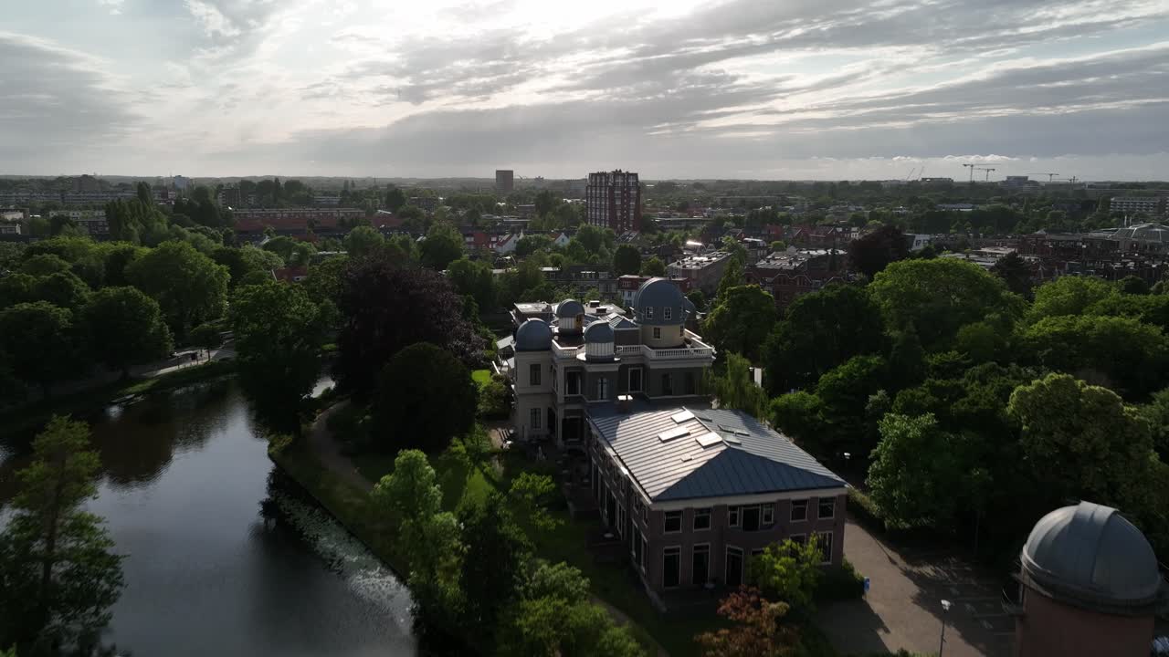 Aerial zoom out from Leiden Observatory domes with the urban landscape of Leiden and cloudy sky in the Netherlands