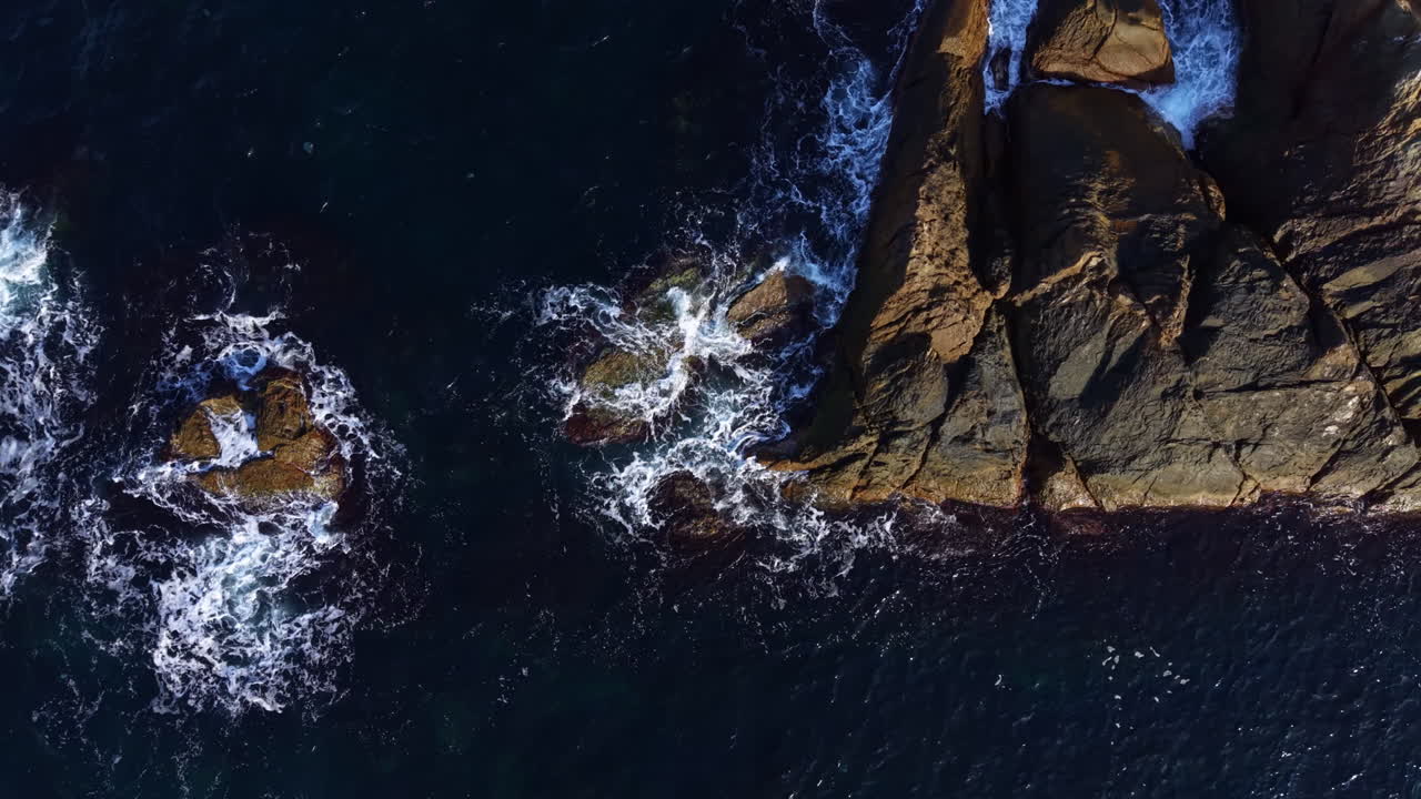 Majestic ocean waves crash against rugged rock formations on a sunny day